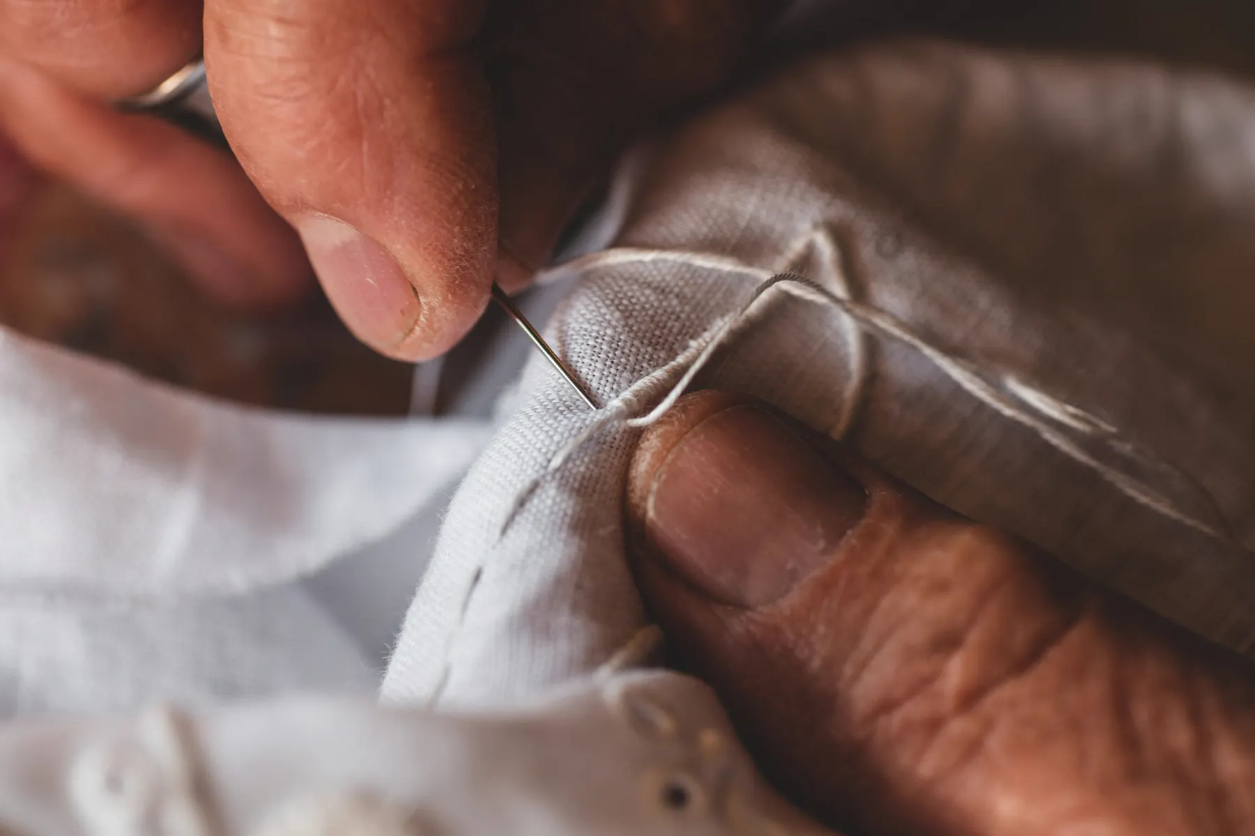 An artisan's hands draw a needle and thread through white cloth