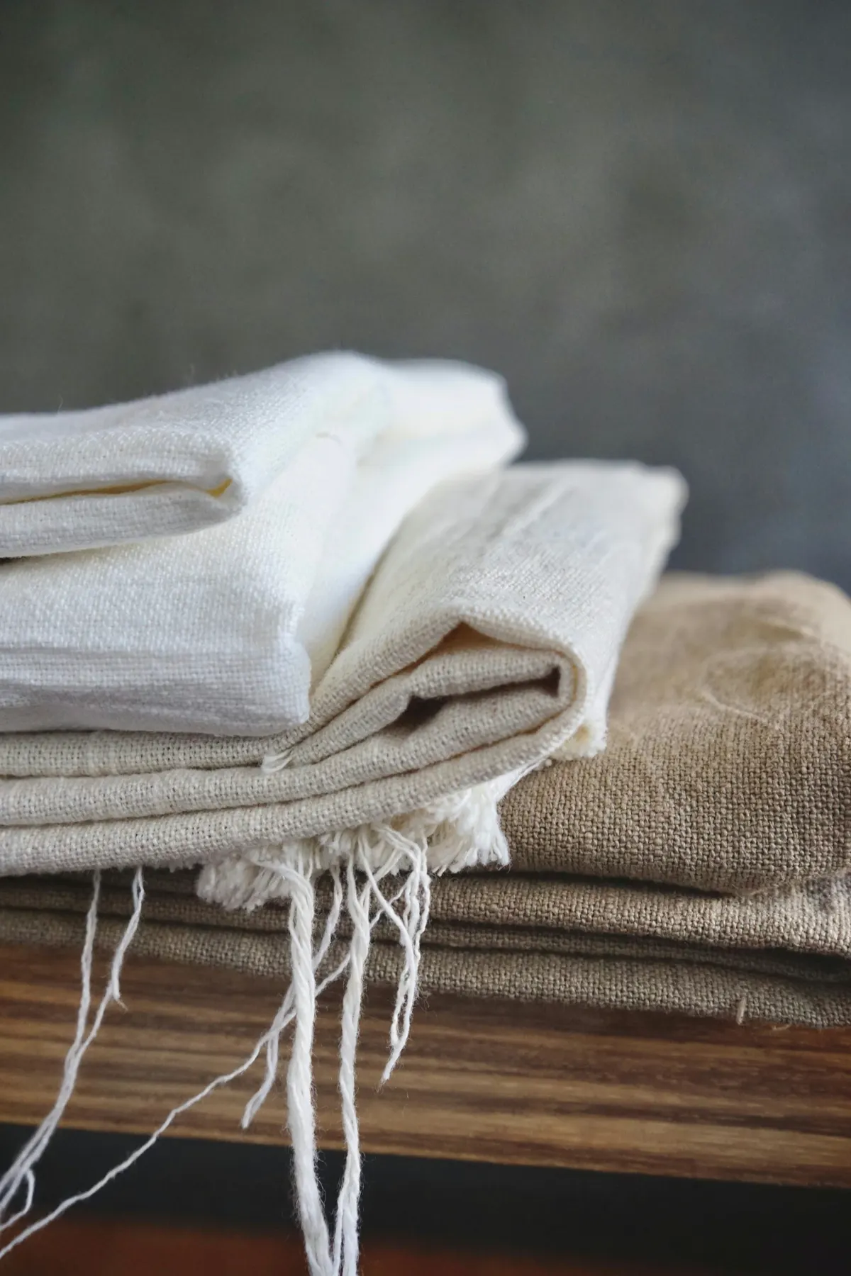 Folded natural and white cloth stacked on a wooden shelf, loose threads at the edge