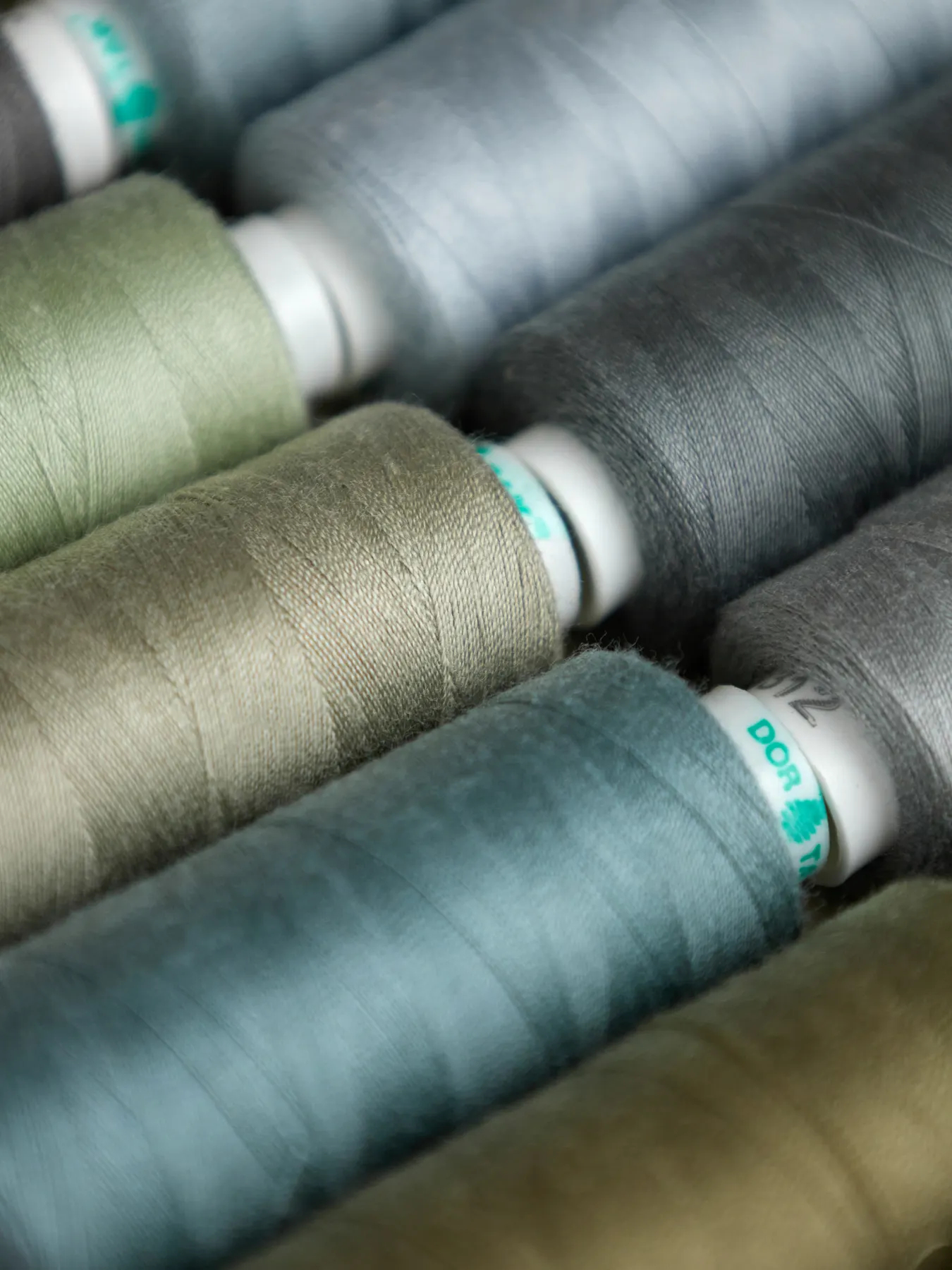 Spools of thread in muted greens and greys stacked on their sides
