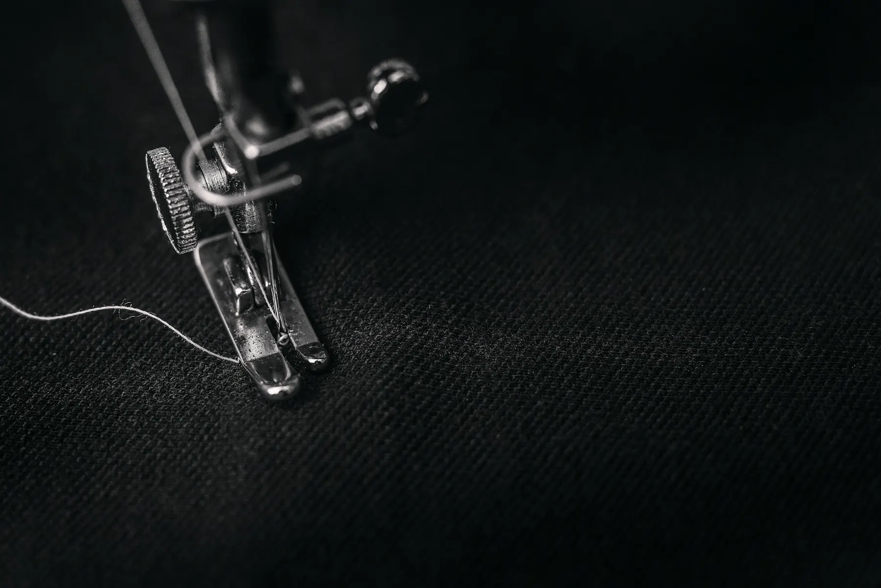 A sewing machine presser foot on dark cloth, one loose thread beside it